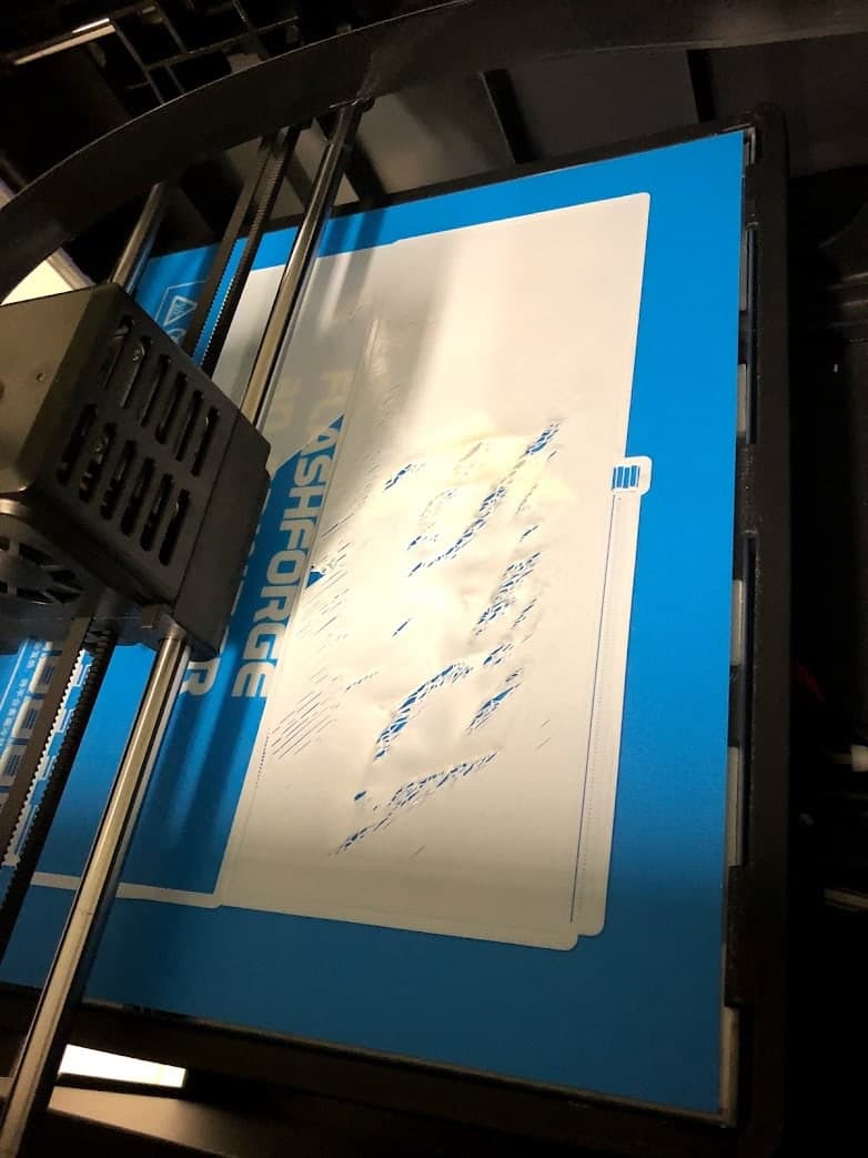 An unsuccessful 3D print on the printer bed, with incomplete material across the white component.